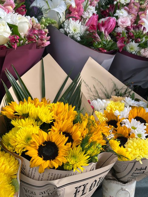 Several bouquets of fresh flowers arranged for floral gift and flower delivery, featuring vibrant yellow sunflowers with dark centers, white daisies, and yellow carnations wrapped in cream and white p
