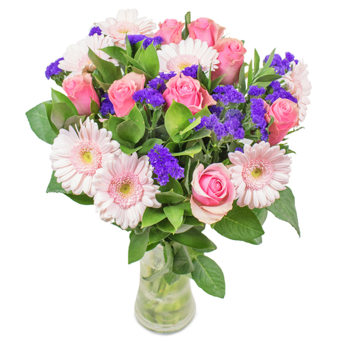 An elegantly vivid floral arrangement crafted by Newsouthgate's talented florists, this bouquet is showcased in a clear glass vase set against a pure white background. At the heart of the piece is a mix of seven to nine blush and medium pink roses, some tightly coiled and others just beginning to reveal their spiral petals, bursting with classic form and gentle allure. Clusters of five to seven pale pink Gerbera daisies with prominent, softly luminous faces sit alongside, their nearly white centres drawing in the morning light. Drifted throughout the bouquet are sprigs of rich purple statice that add a captivating textural contrast-each delicate, papery cluster reminiscent of the seasonal wildflowers found near Brunswick Park. Lush, dark green foliage offers a foundation of abundance and vitality, grounding the pastel hues and recreating the lushness of local park gardens. The transparent vase holds the bouquet upright, water glimmering at the base, signalling a fresh Newsouthgate flower delivery or a beautifully thought-out gift. This arrangement, ideal for birthdays, Mother's Day, or simply bringing fresh colour to a North London home or office, is designed to convey enduring joy, celebration, and affectionate connection.